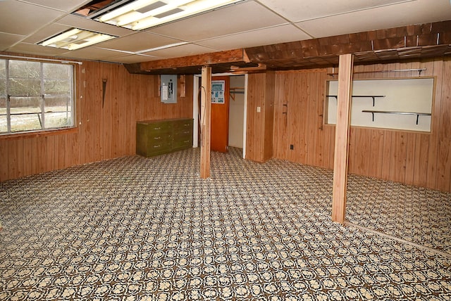 basement with electric panel, wooden walls, and a paneled ceiling