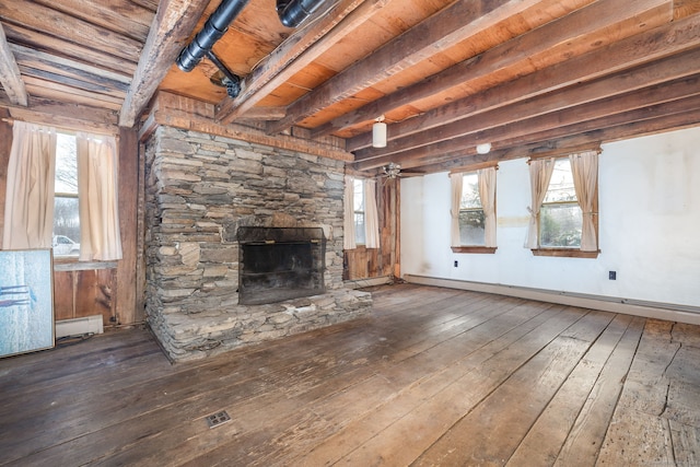 unfurnished living room featuring a wealth of natural light, dark wood-type flooring, baseboard heating, a stone fireplace, and beamed ceiling