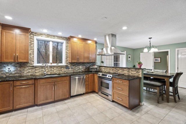 kitchen with island exhaust hood, stainless steel appliances, sink, decorative light fixtures, and dark stone countertops