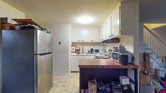 kitchen with wood counters, white cabinetry, stainless steel refrigerator, and sink