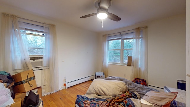 bedroom with light hardwood / wood-style floors, a baseboard radiator, multiple windows, and ceiling fan