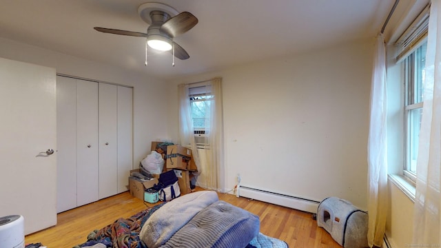 bedroom featuring ceiling fan, light hardwood / wood-style floors, a baseboard heating unit, and a closet