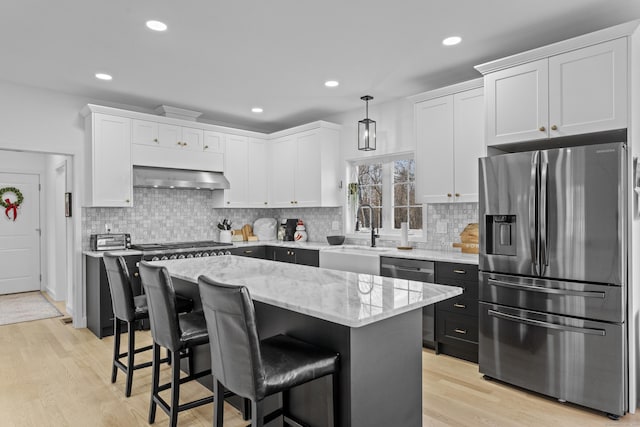 kitchen featuring sink, appliances with stainless steel finishes, white cabinets, a kitchen island, and exhaust hood