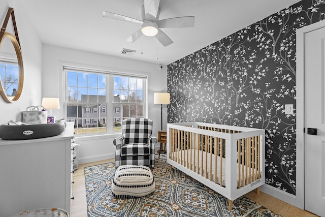 bedroom with light hardwood / wood-style flooring, a nursery area, and ceiling fan