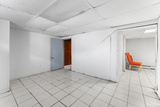 basement with a drop ceiling, light tile patterned floors, and a baseboard heating unit