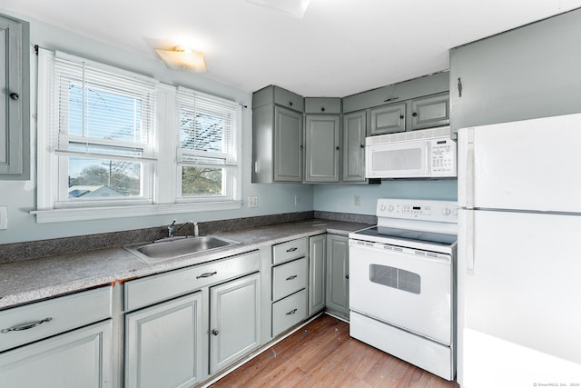 kitchen with gray cabinetry, hardwood / wood-style floors, white appliances, and sink