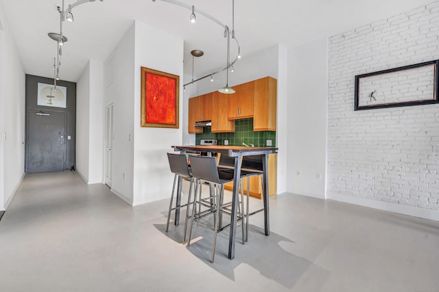 kitchen featuring a high ceiling, brick wall, pendant lighting, a kitchen bar, and decorative backsplash