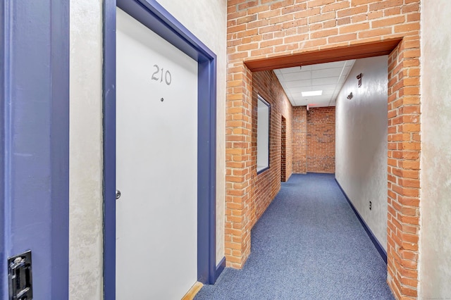 corridor featuring dark carpet and brick wall