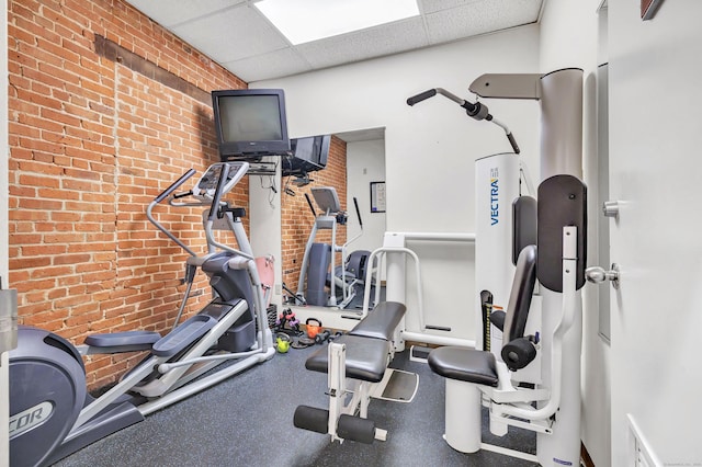 workout area featuring a drop ceiling and brick wall