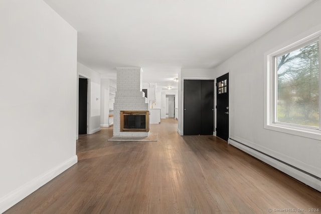 unfurnished living room with hardwood / wood-style floors, a brick fireplace, and a baseboard radiator