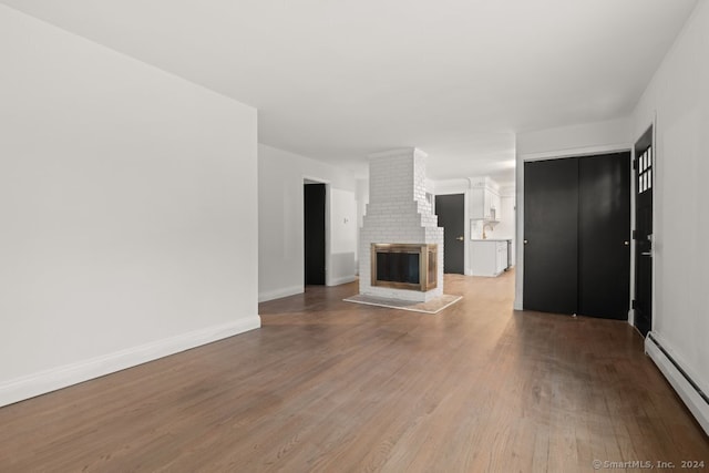 unfurnished living room featuring wood-type flooring, a brick fireplace, and a baseboard heating unit