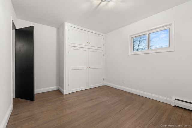 unfurnished bedroom featuring a baseboard radiator, a closet, and dark wood-type flooring