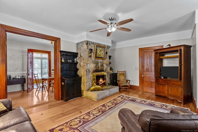 living room featuring ceiling fan, a stone fireplace, and light hardwood / wood-style flooring