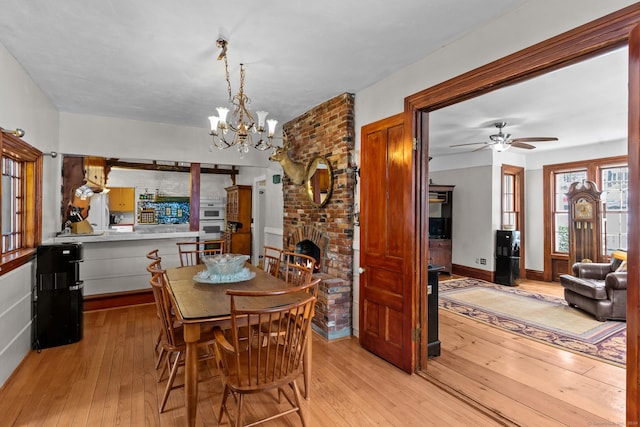 dining area with ceiling fan with notable chandelier, light wood-type flooring, brick wall, and a brick fireplace