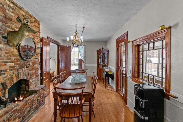 dining room featuring a fireplace, a textured ceiling, light wood-type flooring, and a chandelier