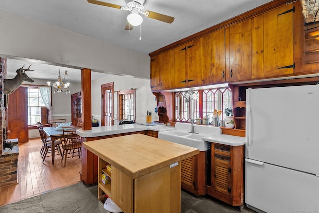 kitchen with sink, dark wood-type flooring, kitchen peninsula, white fridge, and ceiling fan with notable chandelier