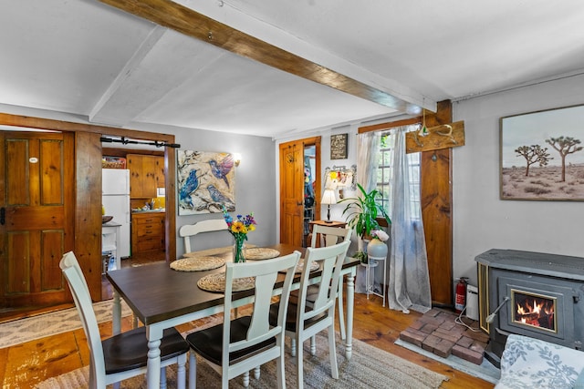 dining space featuring beam ceiling, wood-type flooring, and a wood stove