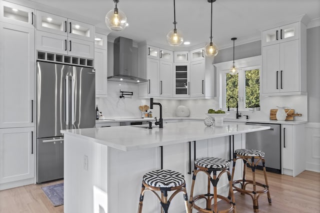 kitchen with wall chimney range hood, crown molding, a center island with sink, white cabinets, and appliances with stainless steel finishes