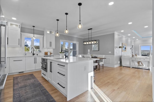 kitchen with a center island, white cabinets, sink, hanging light fixtures, and light hardwood / wood-style floors