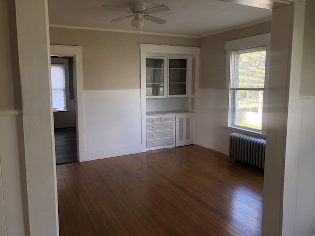 empty room featuring dark hardwood / wood-style floors, radiator, crown molding, and ceiling fan