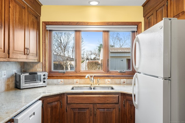 kitchen with tasteful backsplash, light stone countertops, sink, and white appliances