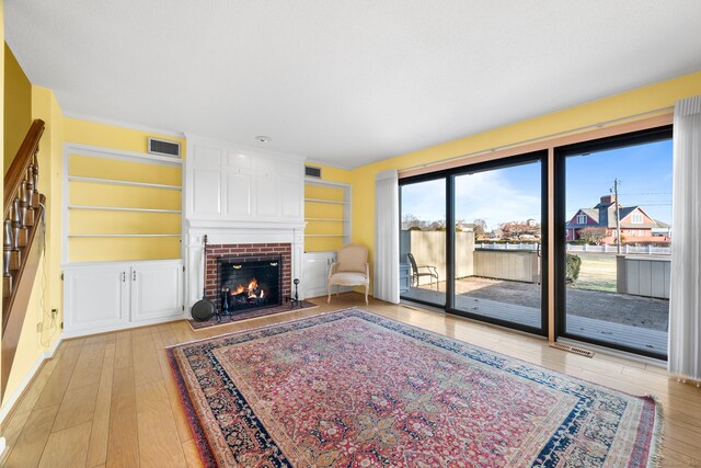 living room with a brick fireplace, built in features, and light hardwood / wood-style flooring