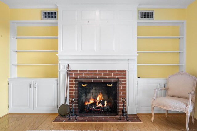 living room featuring built in features, light hardwood / wood-style floors, a brick fireplace, and ornamental molding