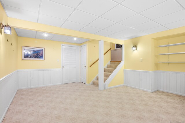 basement with light carpet, built in features, and a drop ceiling