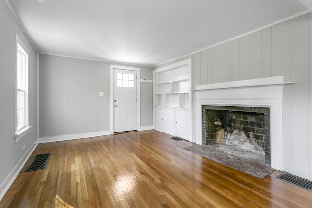 unfurnished living room with wood walls, wood-type flooring, and ornamental molding