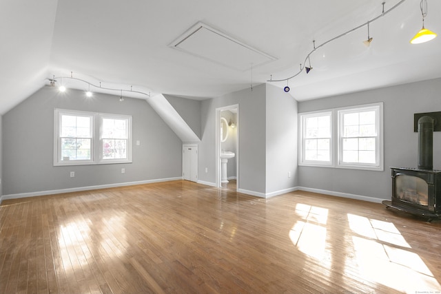 additional living space featuring a wood stove, a wealth of natural light, light hardwood / wood-style floors, and lofted ceiling