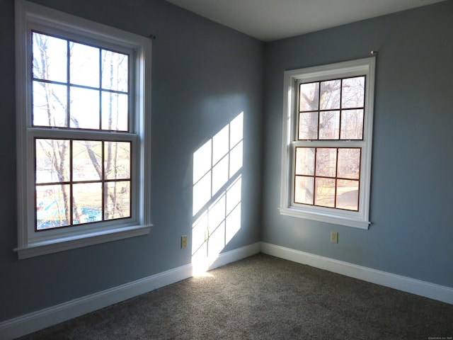 spare room with baseboards and dark carpet