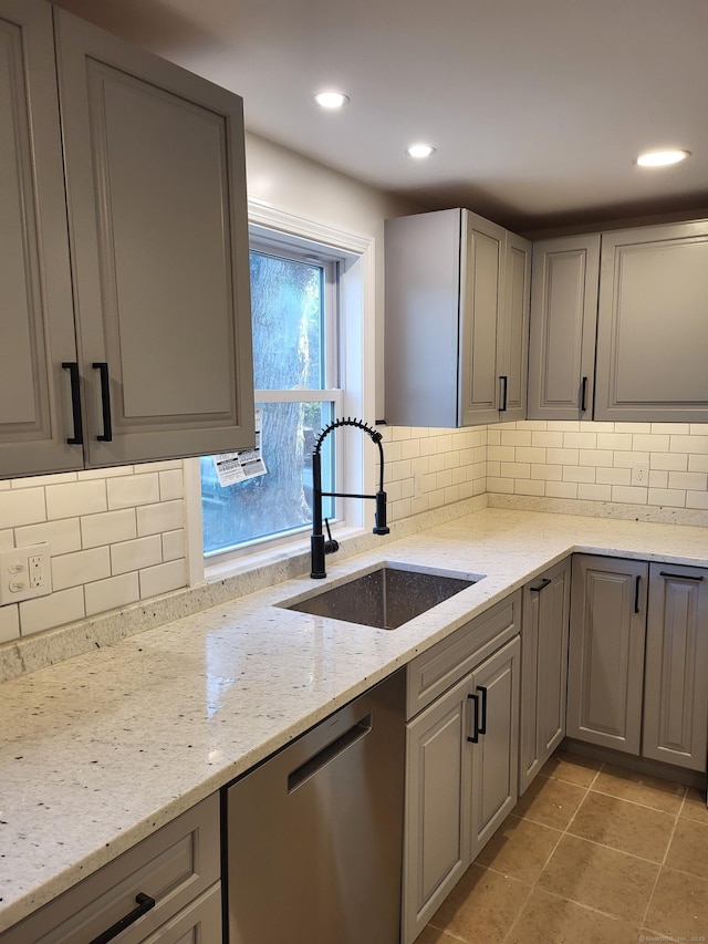 kitchen featuring sink, light stone counters, gray cabinets, dishwasher, and decorative backsplash