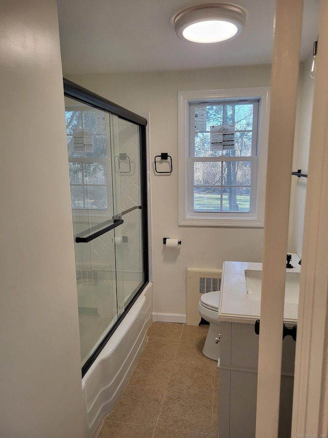 full bathroom with shower / bath combination with glass door, tile patterned flooring, radiator heating unit, vanity, and toilet