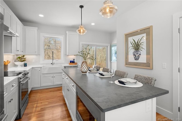 kitchen with sink, stainless steel appliances, white cabinets, a kitchen island, and decorative light fixtures