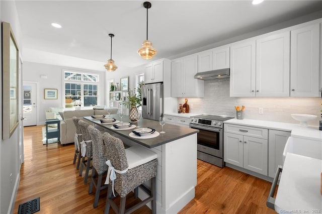 kitchen with pendant lighting, light hardwood / wood-style flooring, appliances with stainless steel finishes, a kitchen breakfast bar, and white cabinets