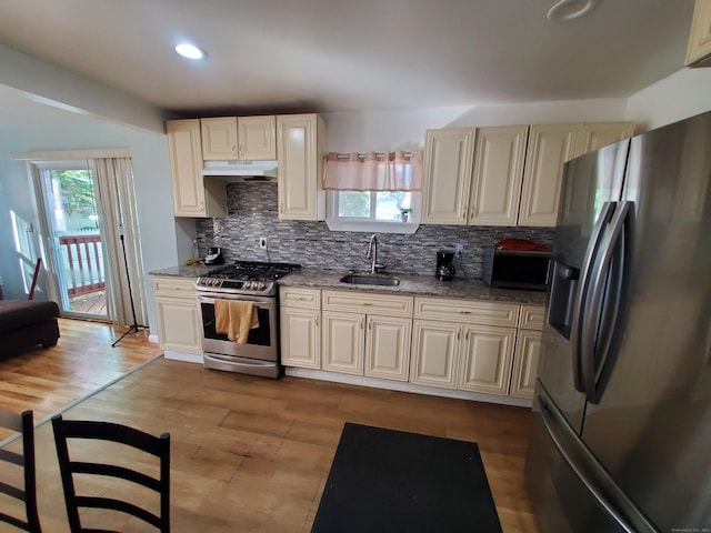 kitchen featuring sink, light stone counters, backsplash, appliances with stainless steel finishes, and light wood-type flooring