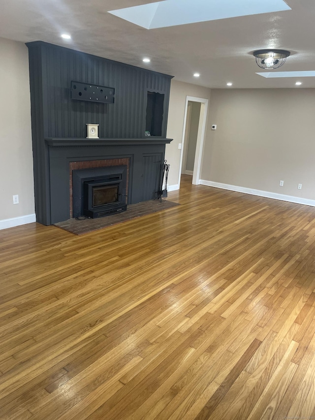 unfurnished living room featuring hardwood / wood-style floors, a skylight, and a wood stove