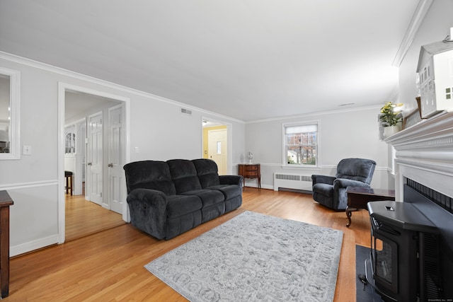 living room with a wood stove, crown molding, radiator heating unit, and light hardwood / wood-style flooring