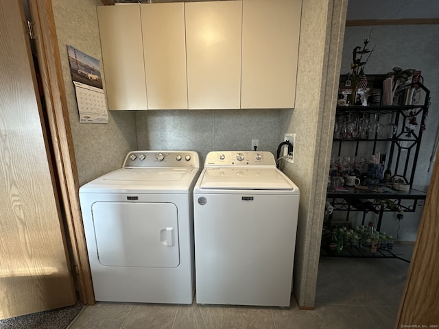 clothes washing area with washing machine and clothes dryer, light tile patterned floors, and cabinets