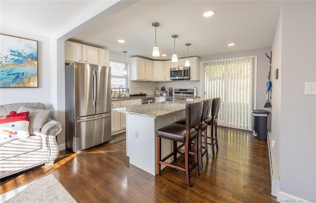 kitchen featuring tasteful backsplash, dark wood finished floors, light stone counters, stainless steel appliances, and a kitchen bar