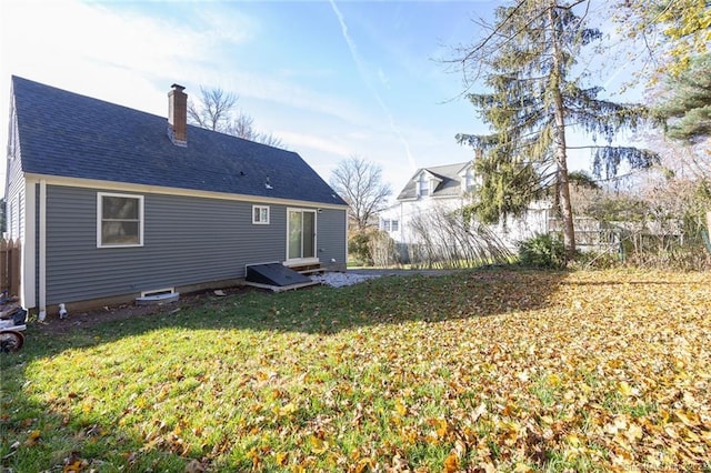 rear view of property featuring a shingled roof, a lawn, and a chimney