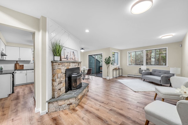 living room featuring a wood stove, a baseboard radiator, and light wood-type flooring