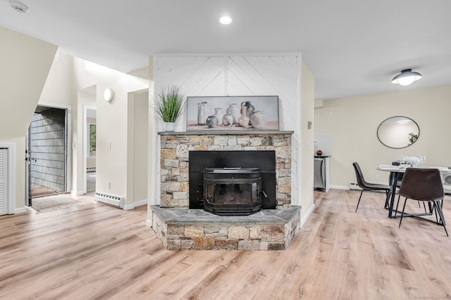 living room with light wood-type flooring, a baseboard radiator, and a wood stove