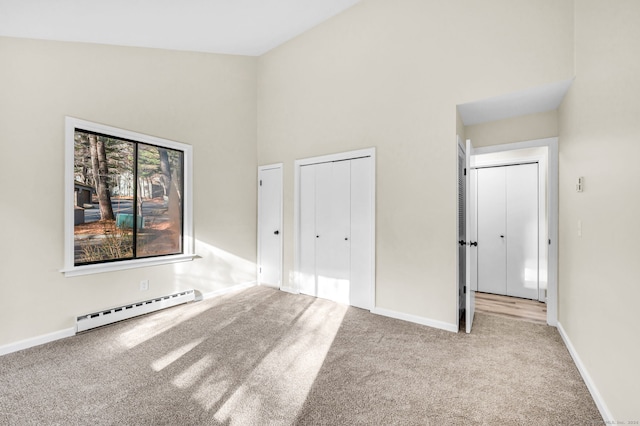 unfurnished bedroom featuring light carpet, a high ceiling, and a baseboard heating unit