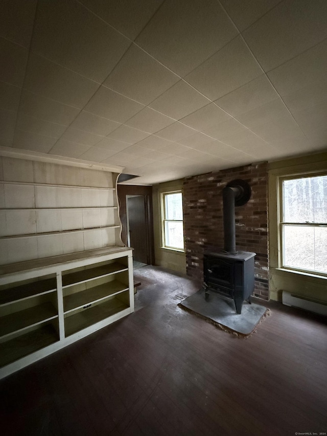 additional living space with baseboard heating, a wood stove, and dark hardwood / wood-style floors