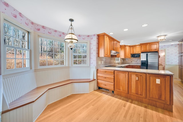 kitchen featuring kitchen peninsula, built in microwave, decorative light fixtures, stainless steel fridge with ice dispenser, and light hardwood / wood-style floors