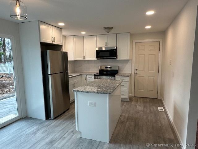 kitchen with stainless steel appliances, white cabinets, a kitchen island, and decorative light fixtures