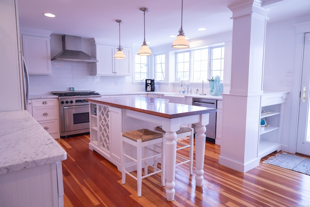 kitchen featuring ornate columns, a center island, dark wood-type flooring, wall chimney range hood, and appliances with stainless steel finishes