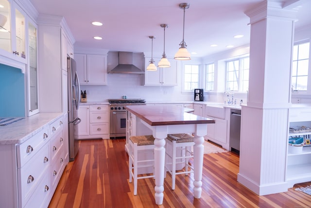 kitchen with white cabinetry, stainless steel appliances, wall chimney range hood, and hardwood / wood-style flooring