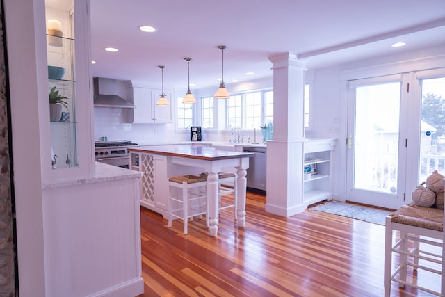 kitchen with white cabinets, wall chimney range hood, a breakfast bar area, light hardwood / wood-style flooring, and stainless steel appliances